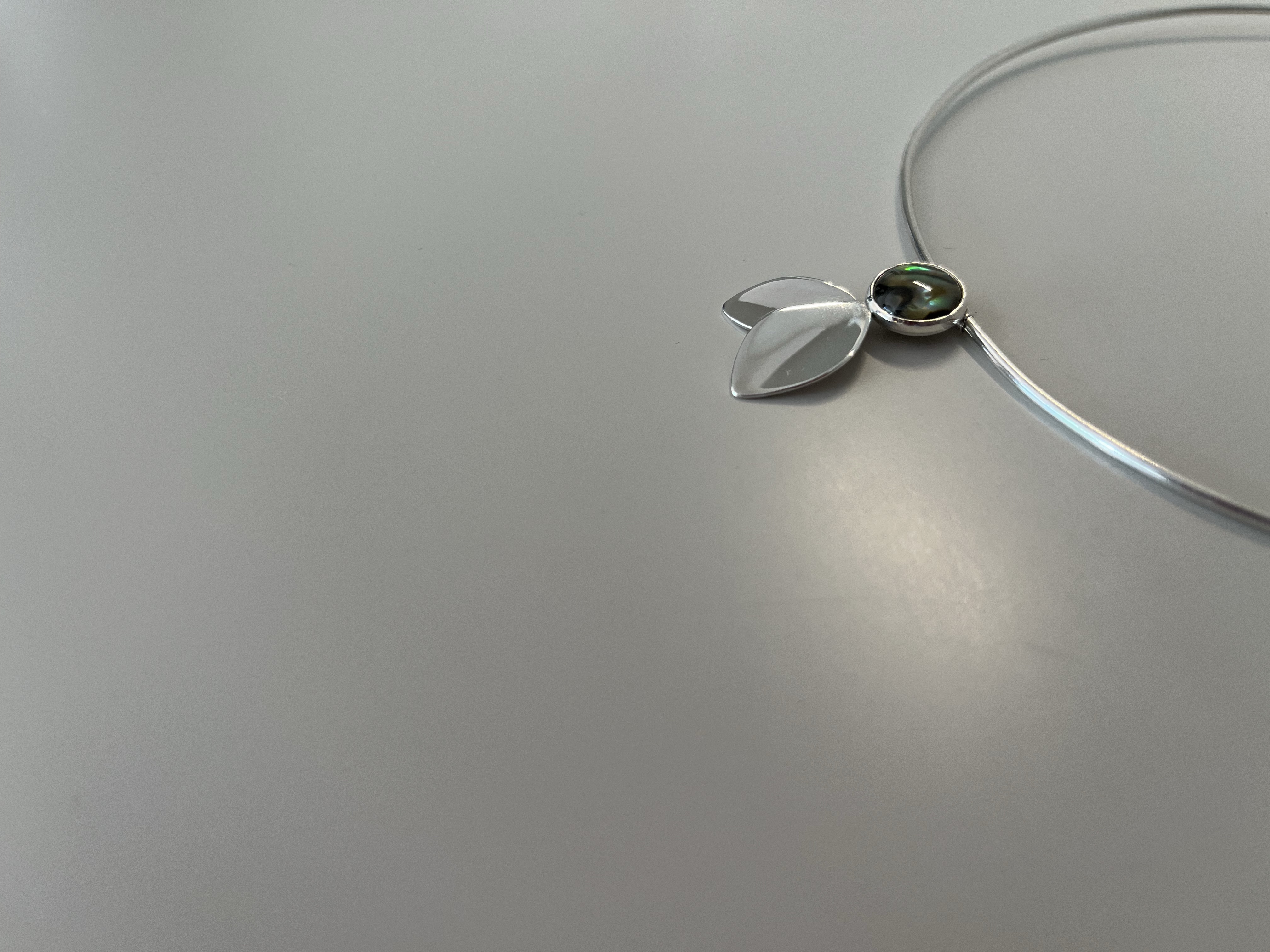 Silver necklace detail with green iridescent stone in soft natural light
